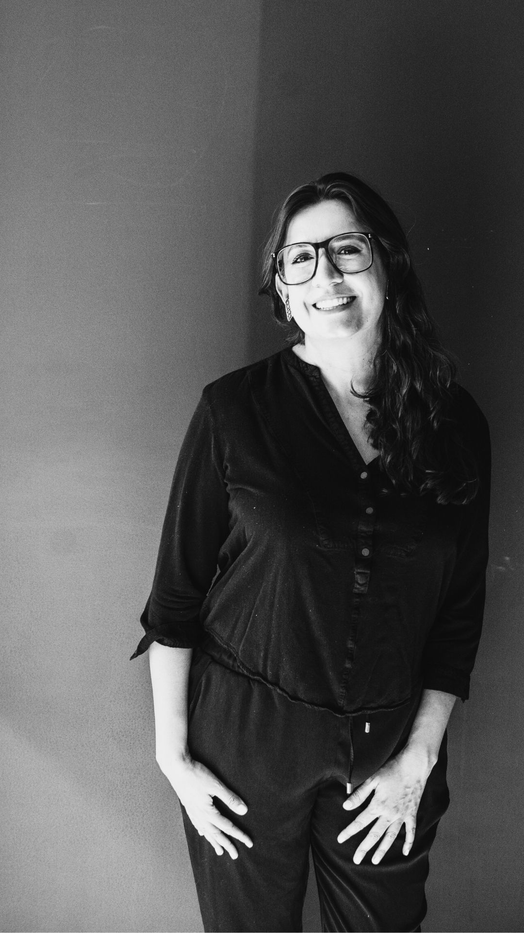 Fotografía en blanco y negro de Itzamá Enríquez Íñiguez, tallerista y profesora de redacción. Ella es una mujer de mediana. En la foto está sonriendo. Lleva gafas de montura gruesa y su cabello, que es onduldado, le cae sobre los hombros. El fondo del retrato es una liso y oscuro.