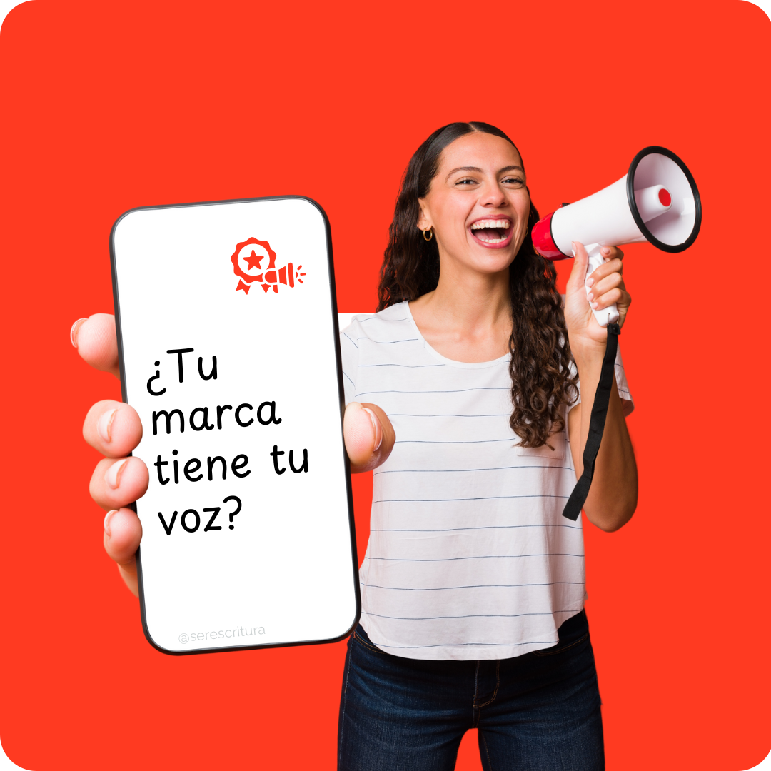 Una mujer joven, con cabello rizado oscuro y una camiseta blanca, sonríe ampliamente mientras sostiene un megáfono blanco y rojo con su mano derecha y un smartphone blanco con la mano izquierda. La pantalla del smartphone muestra el texto en español 2¿Tu marca tiene tu voz?" y un logo en rojo con un sello de calidad y una estrella. El fondo es de color naranja vibrante. La imagen acompaña el curso de redacción de Ser Escritura: "Desarrolla tu voz de marca".
