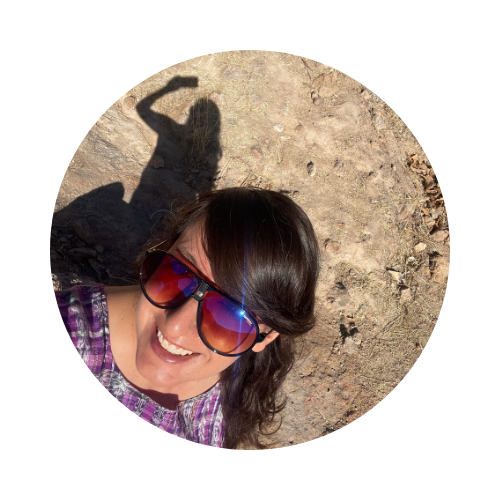 Selfi de la escritora mexicana Itzamá Enríquez Íñiguez. Itzamá es una mujer sonriente de mediana edad. En la foto lleva una blusa artesanal morada y gafas de sol oscuras. En la parte la parte superior de la foto se ve su sombra sobre un terreno rocoso.